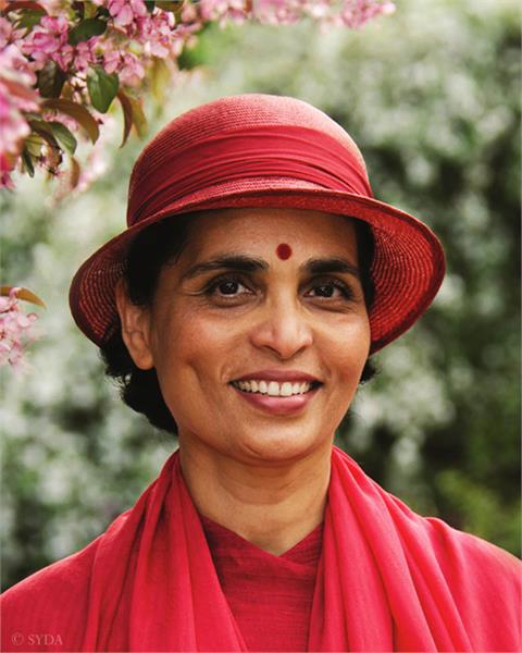 Close up of Gurumayi in red hat against a nature background with pink flowers