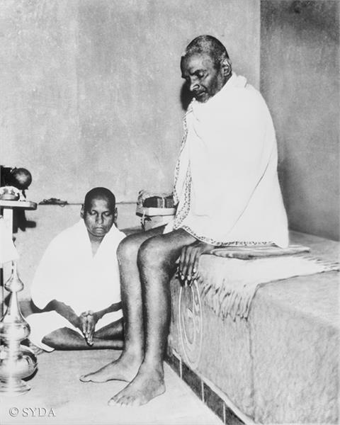Photo of Nityananda sitting on bench next to Baba Muktananda who is meditating