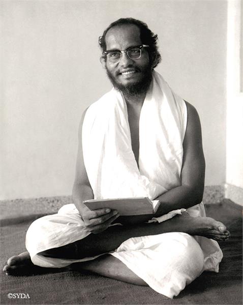 Black and white photo of baba sitting cross legged with a Book in his hand