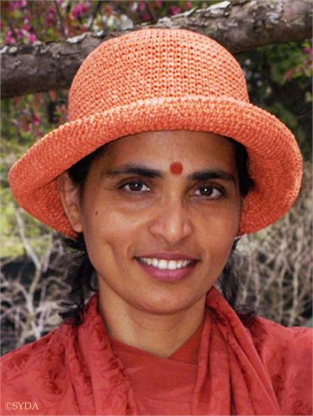 Close up of Gurumayi smiling in an orange hat, with a nature backdrop