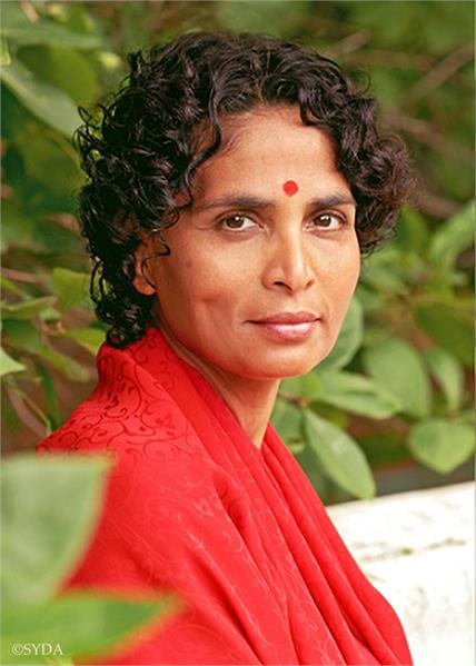 Close up of Gurumayi in red robes, surrounded by green leaves