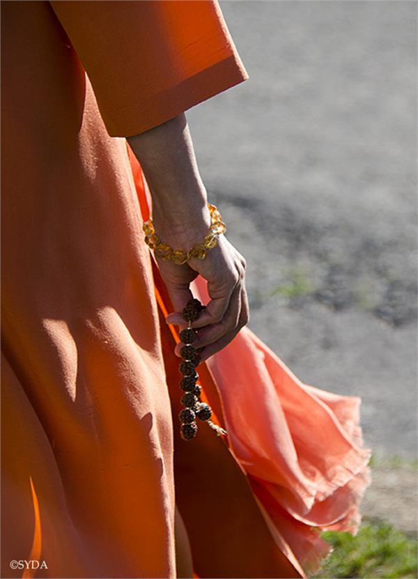 Close up of Gurumayi's hand, walking outside with a japa mala