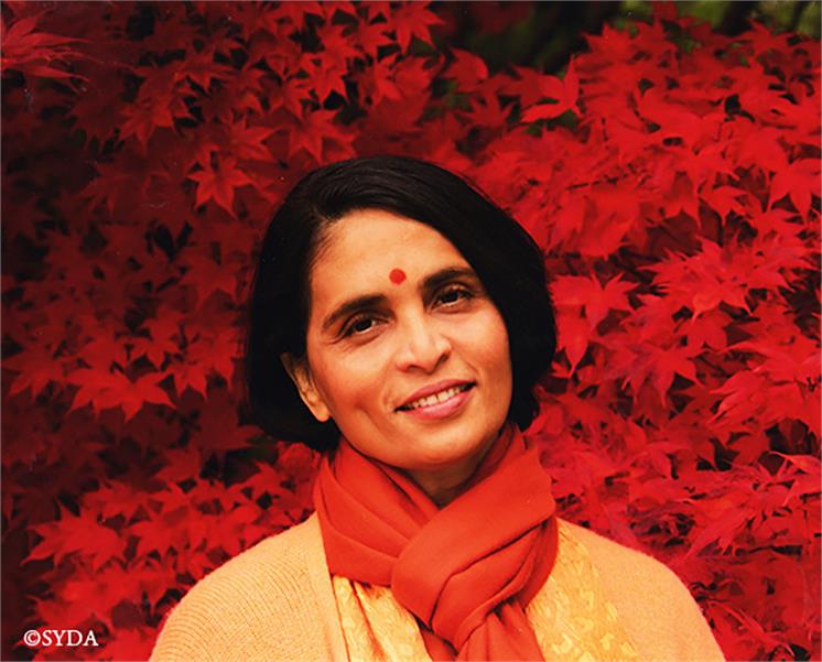 Gurumayi in a red scarf, against a background of red leaves