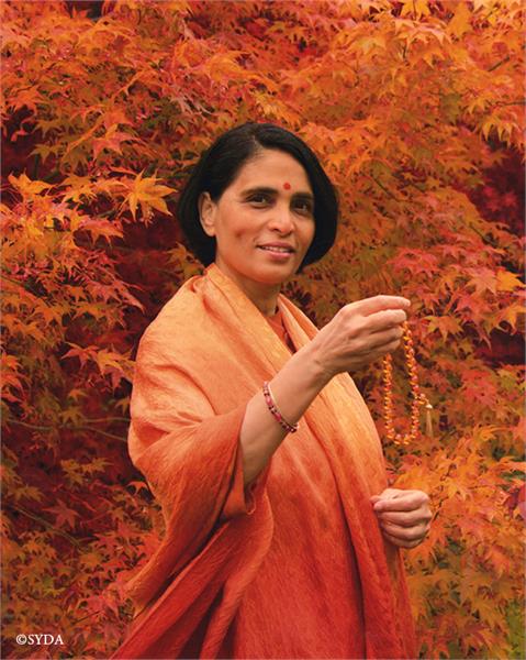 Gurumayi surrounded by autumn leaves, holding out a japa mala
