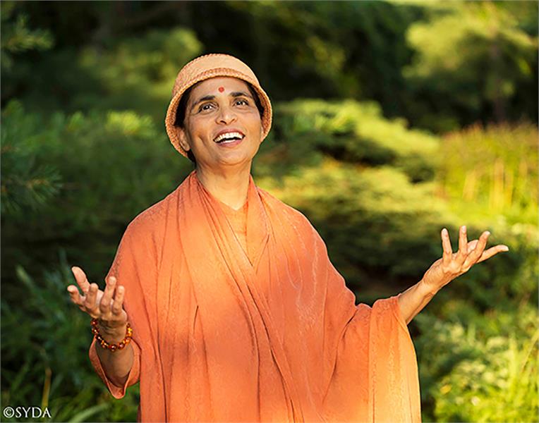 Gurumayi in nature, smiling at the sun and raising her hands to the sky